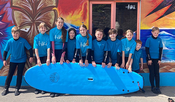 A group of young surfers holding a blue surfboard.