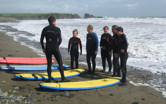 Gemini said A group of people in wetsuits stands on a sandy beach next to several surfboards, listening to an instructor before a lesson.